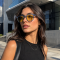 Mulher usando óculos AURA Day Blue com armação azul translúcida e lentes amarelas com filtro de luz azul em ambiente urbano.