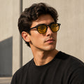 Homem usando óculos NOX Day preto com lentes amarelas e filtro de luz azul, em ambiente urbano com luz natural.