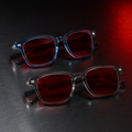 Óculos AURA Night Blue e Smoke com armações translúcidas e lentes vermelhas, posicionados sobre superfície metálica escura com iluminação noturna em vermelho.