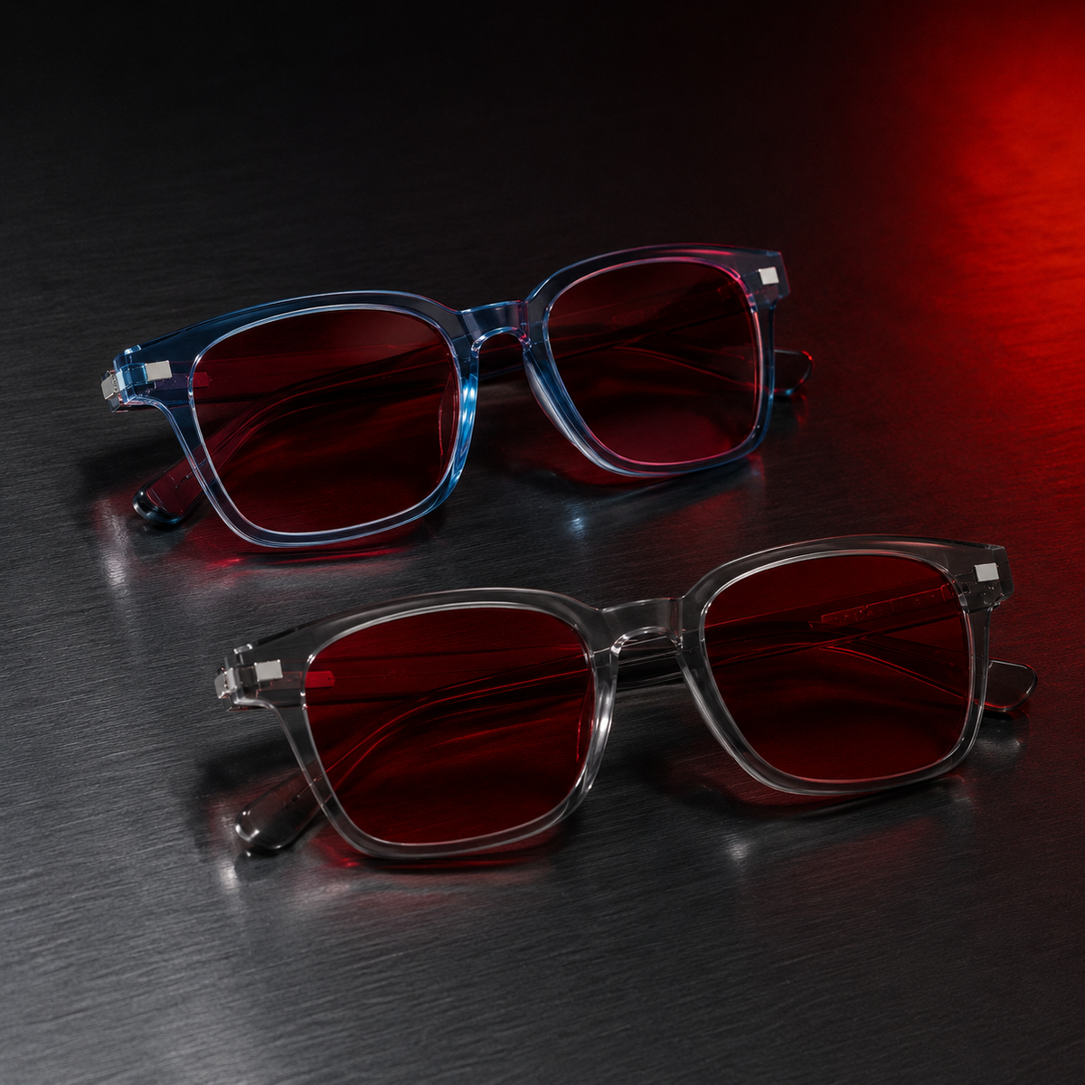 Óculos AURA Night Blue e Smoke com armações translúcidas e lentes vermelhas, posicionados sobre superfície metálica escura com iluminação noturna em vermelho.