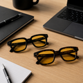 Óculos Vesper Day nas cores Black e Tortoise com lentes amarelas de filtro de luz azul, sobre mesa de escritório com notebook e acessórios de trabalho.
