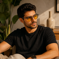Homem usando óculos AURA Day com armação Smoke e lentes amarelas em um ambiente interno moderno, com iluminação natural e decoração minimalista ao fundo.