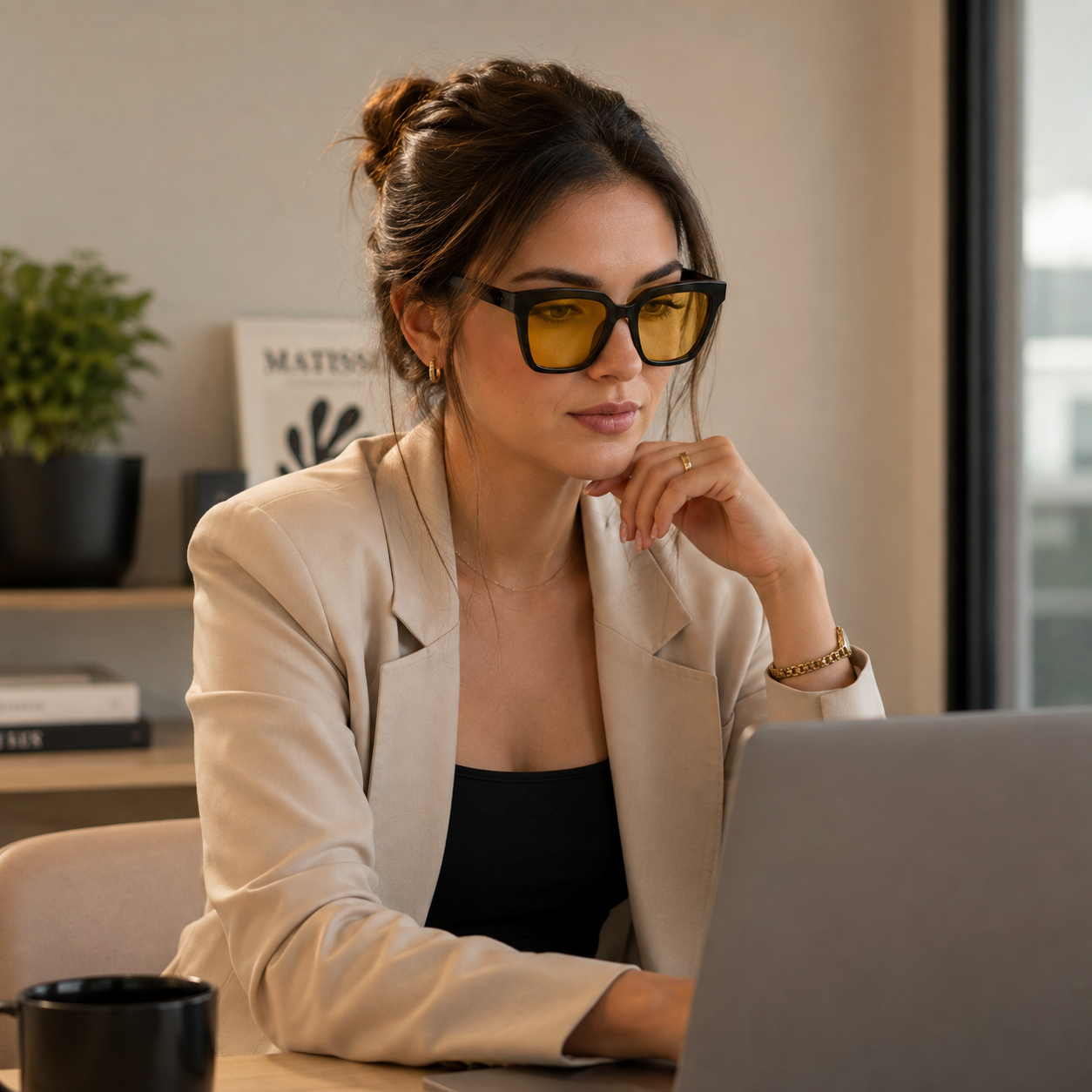 Mulher usando óculos VESPER Day com armação Black e lentes amarelas enquanto trabalha em um laptop em um ambiente moderno e aconchegante, com iluminação natural e decoração minimalista.
